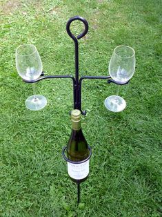 a wine bottle holder with three glasses on it in the middle of some green grass