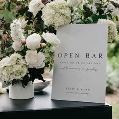 an open bar sign sitting on top of a table with white flowers in vases