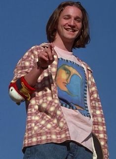 a man holding a skateboard in his right hand and wearing a shirt with a painting on it