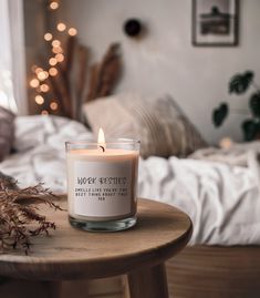 a candle sitting on top of a wooden table in front of a bed with lights