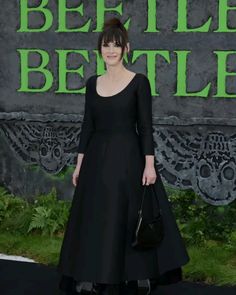 a woman in a black dress standing on a black carpet with green lettering behind her