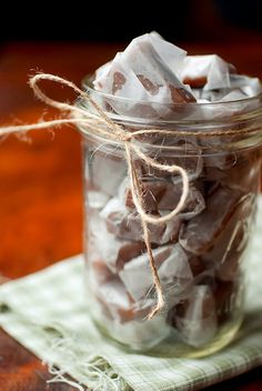 a glass jar filled with chocolate pieces on top of a green cloth next to a wooden table