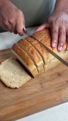 a person cutting bread on top of a wooden cutting board