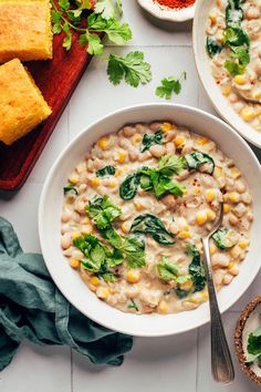 two bowls of white bean soup with corn, spinach and parsley on the side