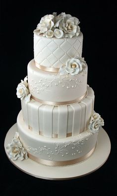 a three tiered wedding cake with white flowers on the top and sides, sitting on a platter