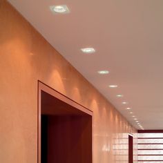 an empty hallway with red doors and lights on the ceiling is seen in this image