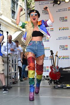 a woman in high waisted shorts and colorful boots on stage with her arms up