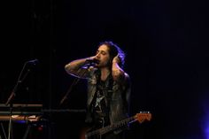 a man standing in front of a microphone while holding a guitar up to his ear