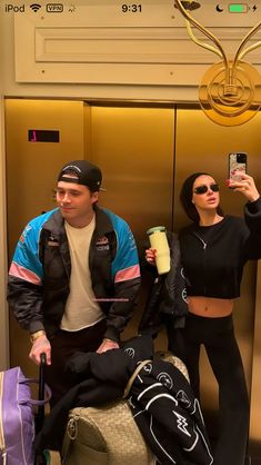 a man and woman standing next to each other in front of an elevator holding up their cell phones