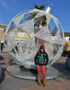 a woman standing in front of a large metal ball with a christmas tree on it