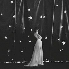 black and white photograph of woman standing in front of curtain with stars on the wall