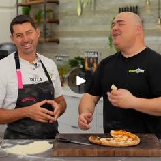 two men standing in front of a pizza on a cutting board