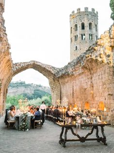 an outdoor dining area with people sitting at tables in front of stone walls and arches