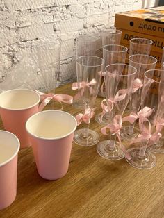 pink cups with bows are lined up on a wooden table next to a cardboard box