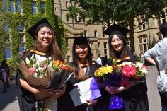 three women in graduation gowns holding bouquets and flowers on the side of a road