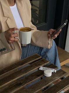 a woman sitting at a table with a cup of coffee and cell phone in her hand