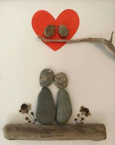 two rocks sitting on top of a piece of driftwood next to a red heart