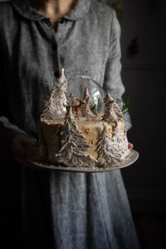 a person holding a plate with a cake on it in the shape of trees and snow flakes