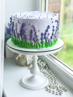 a white cake with purple flowers on it sitting in front of a window sill