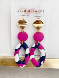 a pair of pink, blue and white earrings hanging from a hook on a wall