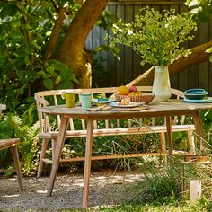 a wooden table with plates and cups on it in the middle of a garden area