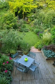 an outdoor table and chairs on a wooden deck surrounded by trees, shrubs and flowers