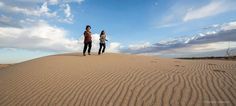 two women are standing on top of a sand dune