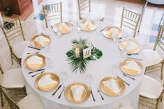 a white table topped with lots of gold plates and silverware covered in greenery