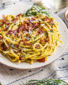 a white plate topped with pasta covered in cheese and bacon next to a bowl of seasoning