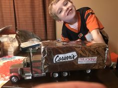 a young boy sitting in front of a toy truck on top of a wooden table