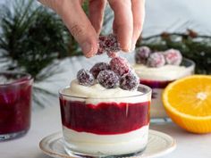 someone is dipping some food into a small glass bowl with berries on top and oranges in the background