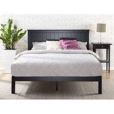 a bed with a black headboard and foot board next to a plant in a white room