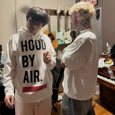 two people standing next to each other in front of a piano and guitar case with hood by air written on it