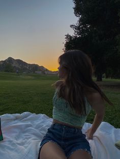 a young woman sitting on top of a blanket next to a bottle of beer in a park