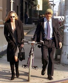 a man and woman walking down the street with a bicycle in hand while wearing business attire