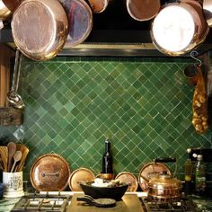 pots and pans are hanging from the ceiling in a kitchen with green tiled walls