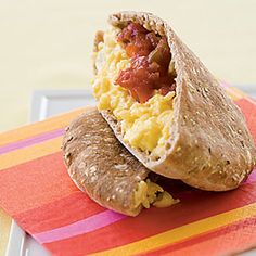 two breakfast burritos sitting on top of a colorful place mat next to each other