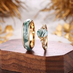 two wedding rings sitting on top of a wooden stand next to each other, one with green and white marble inlays