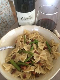 a white bowl filled with pasta and asparagus next to a bottle of wine