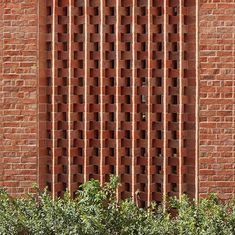 a red brick building with vertical lines on the side and bushes in front of it