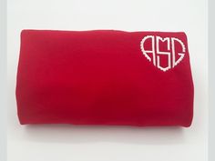 a red pillow with a heart embroidered on the front and initials on the back, sitting on a white surface