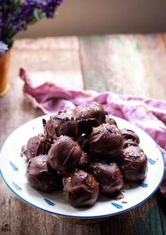 a plate filled with chocolate covered donuts on top of a wooden table next to purple flowers