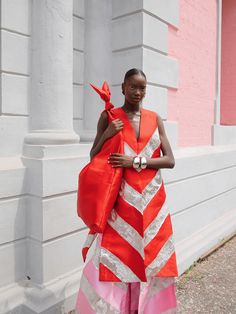 a woman in an orange and white striped dress holding a red bag while standing next to a building