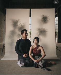 a man and woman sitting on the ground in front of a backdrop