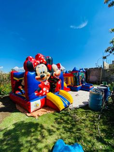 an inflatable mickey mouse bouncer is on the grass near a blue tarp