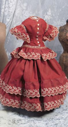 a red dress with white flowers is sitting on a table next to two wooden mannequins