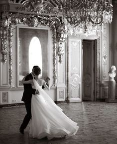 a bride and groom dance together in an ornate room with chandeliers on the ceiling