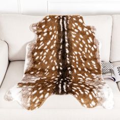 a white and brown animal print rug sitting on top of a couch next to a pillow