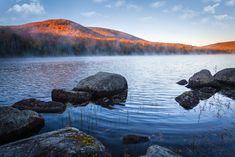 a lake surrounded by rocks and trees in the background, with mountains in the distance