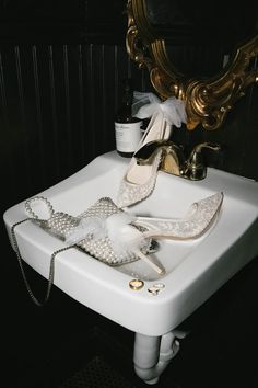 a pair of white high heeled shoes sitting on top of a sink next to a mirror